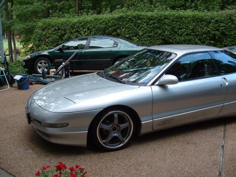 1993 Ford Probe - A silver 1993 Ford Probe GT is parked on a driveway next to a green sedan, with a hedge in the background.