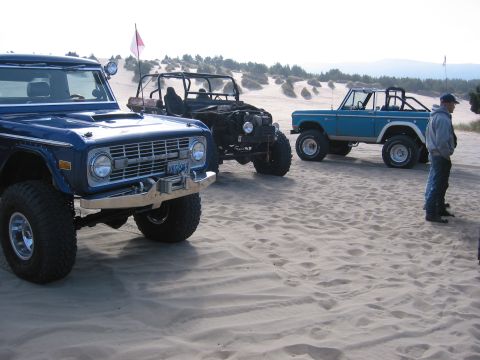 1991 Ford Explorer - Three off-road vehicles parked on sand dunes under a clear sky.