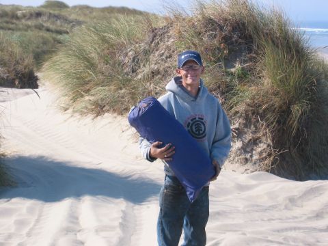 1991 Ford Explorer - A person stands on a sandy beach, holding a rolled-up sleeping bag, with dunes and the ocean in the background.