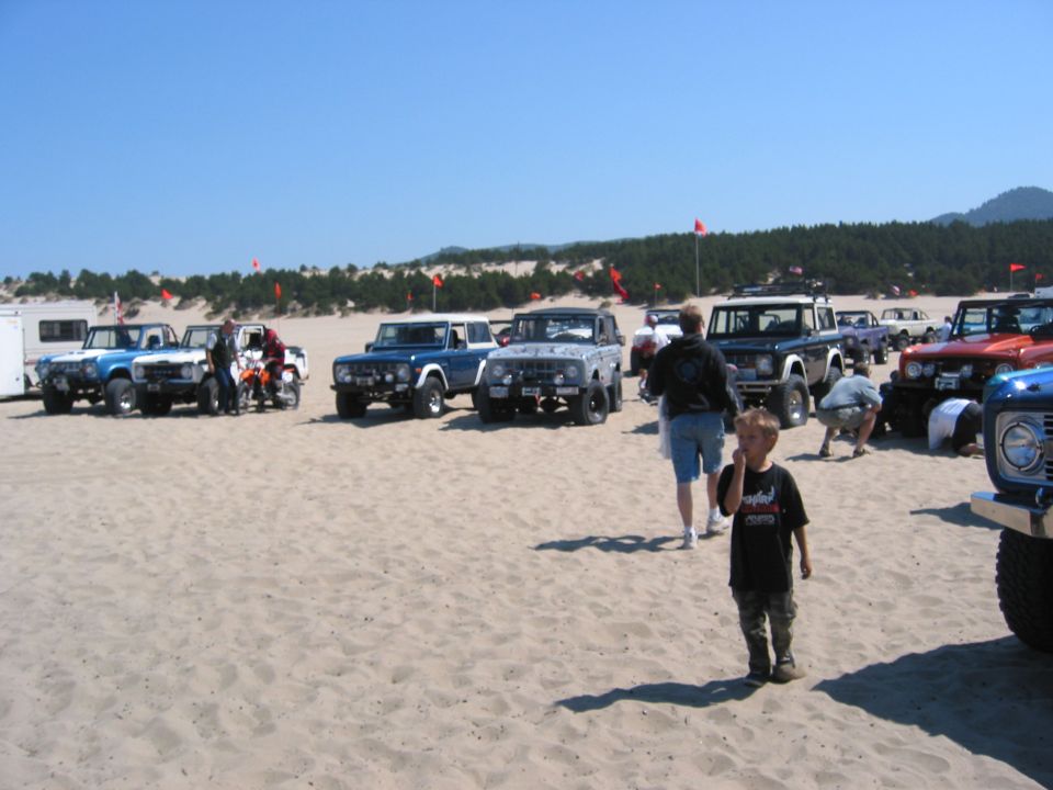 Row of early Ford Broncos parked on sand dunes with orange safety flags