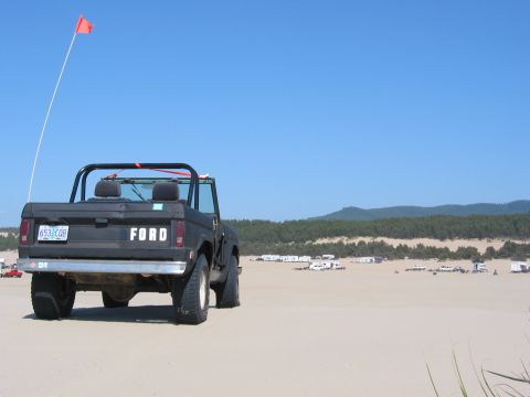 1991 Ford Explorer - A black Ford Bronco is parked on sand dunes with other vehicles in the background under a clear blue sky.