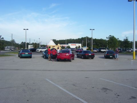 1994 Ford Probe - Several cars are parked in a lot on a sunny day, with people standing around some of the vehicles.