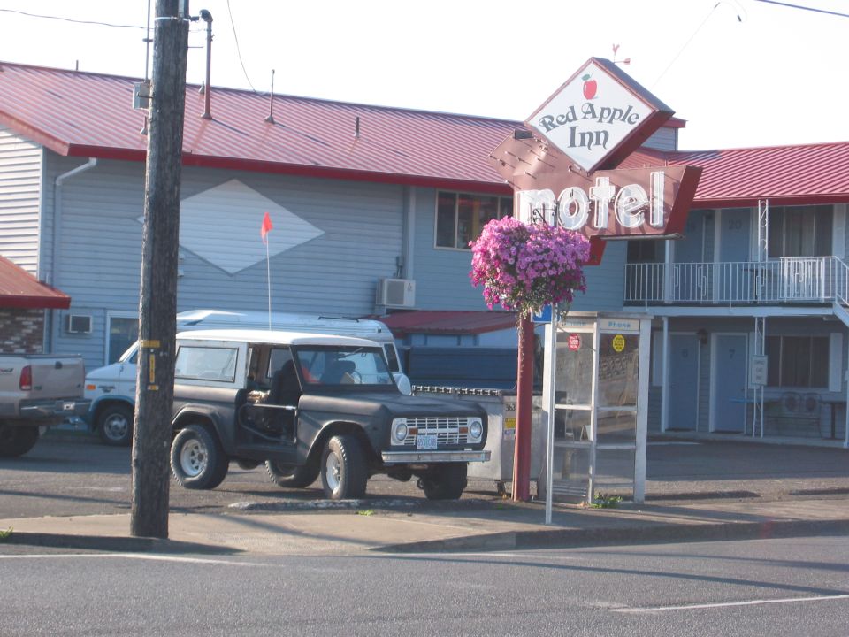 Ford Bronco parked outside a motel with its door open. Another truck and van are visible