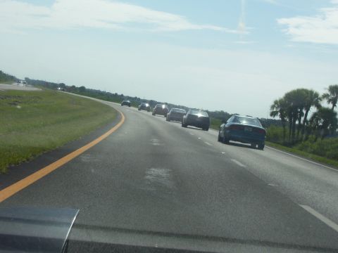 1994 Ford Probe - A line of cars travels down a highway under a partly cloudy sky.