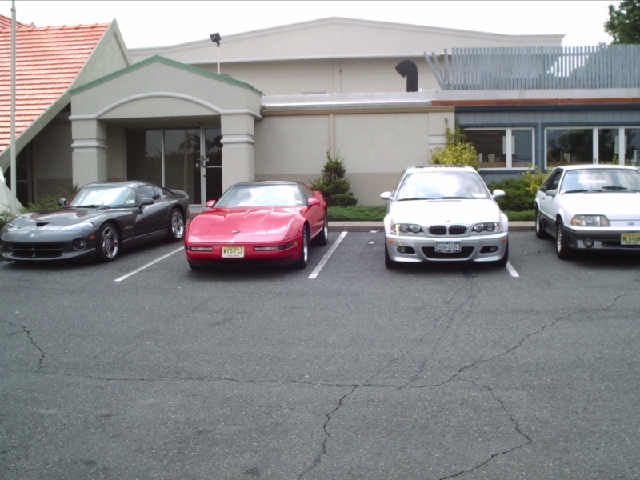 Four cars parked in a lot: a dark gray Dodge Viper, a red Chevrolet Corvette, a silver BMW, and a white Ford Mustang