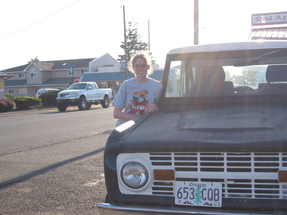 Person leaning on front of old Ford Bronco. White pickup truck in background