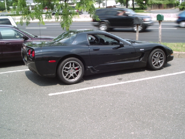 Black C5 Corvette parked in a lot, another car next to it, traffic in background