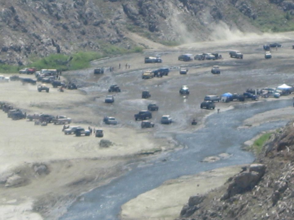 Many off-road vehicles gathered in a muddy, rocky terrain with a stream