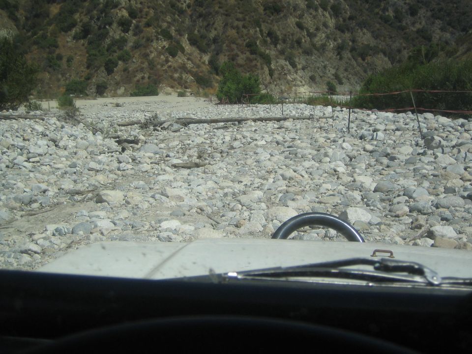 Steering wheel and hood of a light-colored vehicle driving on a rocky, dry riverbed