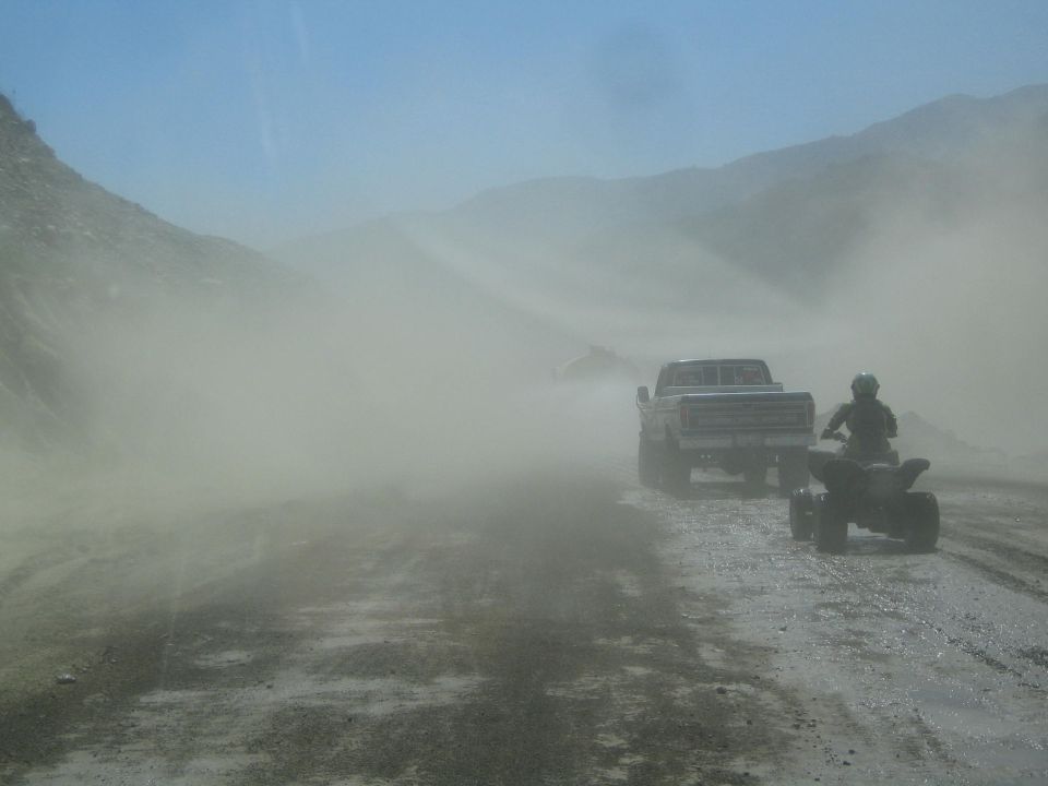 Pickup truck and ATV driving on a dusty road with mountains in the background