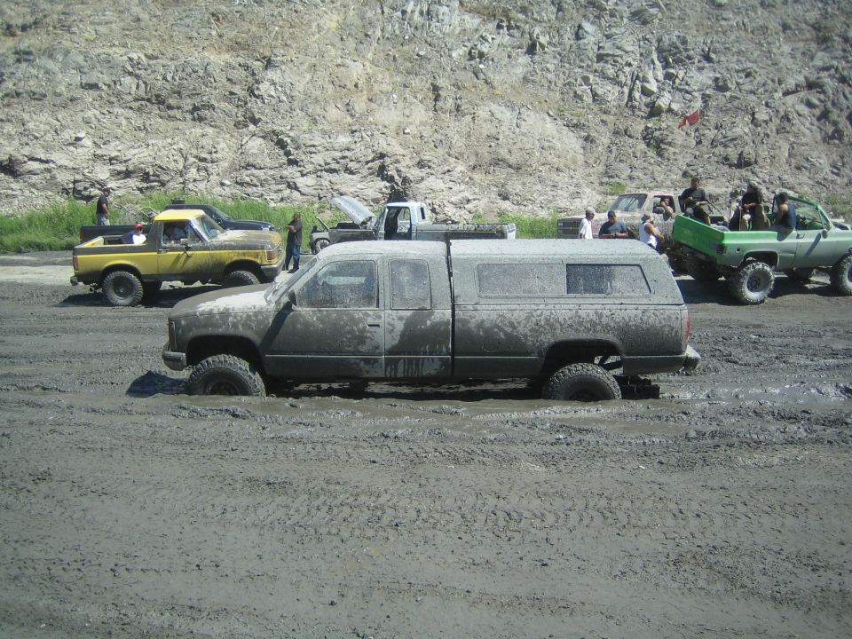 Mud-covered pickup truck with a camper shell stuck in mud, side view