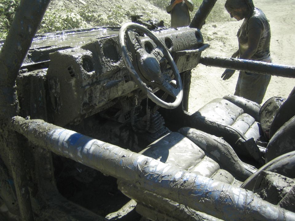 mud-covered interior of a vehicle with steering wheel and seats visible, people in background