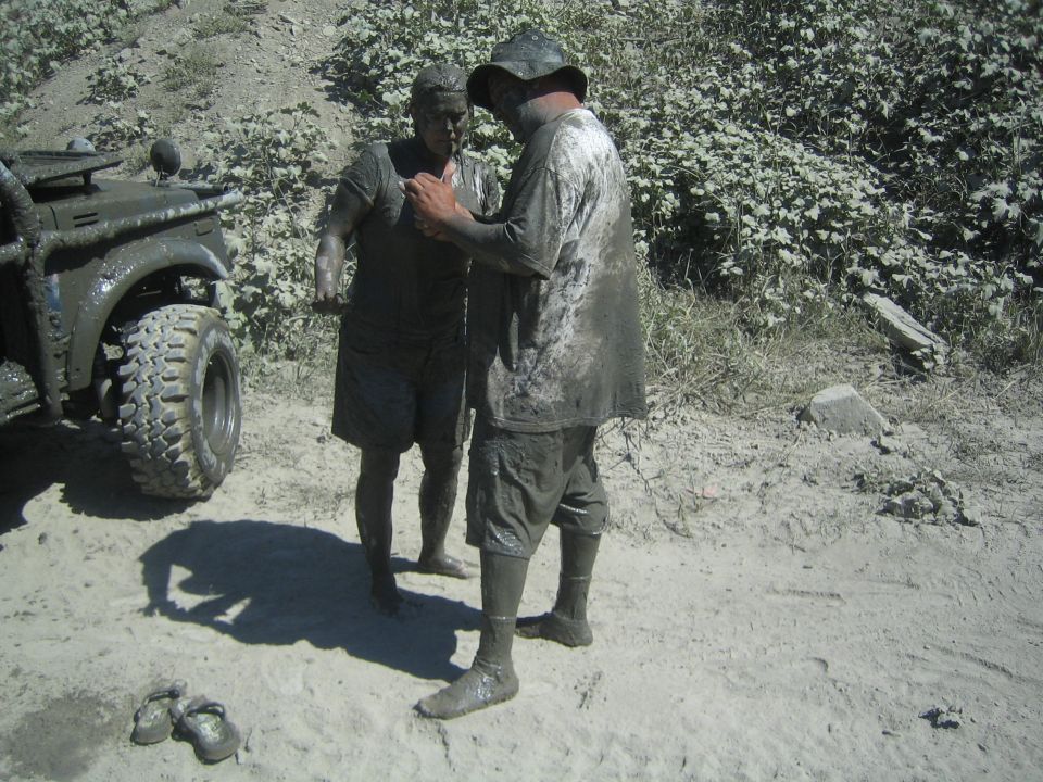 two people covered in mud next to a muddy off-road vehicle