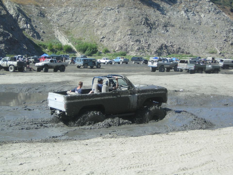 Several off-road trucks stuck in mud with people inside. Mountains in background