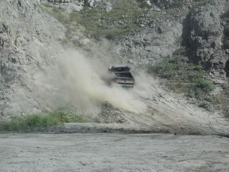 Gray pickup truck kicking up dust while driving down a dirt slope
