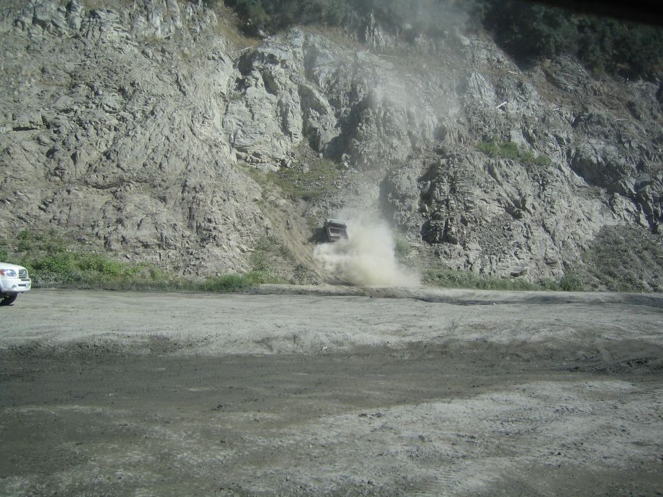 Truck kicking up dust on a dirt road next to a rocky cliff