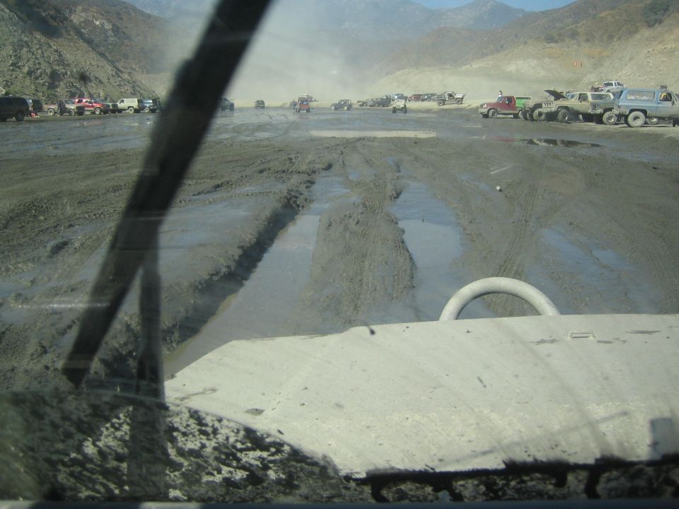 Muddy off-road terrain with many vehicles parked and driving in the distance