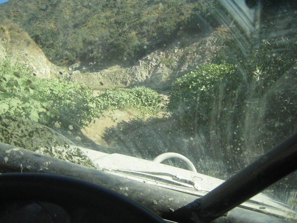 View from inside a dirty off-road vehicle, looking out the windshield at a steep, overgrown dirt path