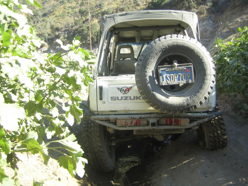 White Suzuki Samurai rear view on a dirt trail with a spare tire mounted on the back