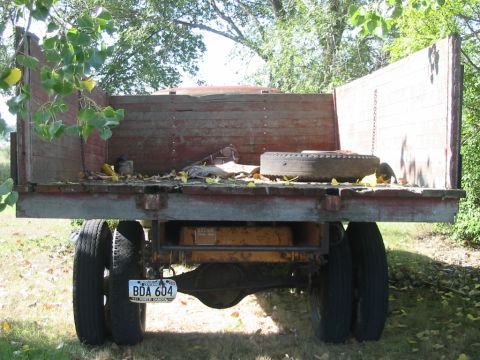 1951 Chevrolet C/K Pickup - Rear view of a flatbed truck with a worn wooden bed and dual rear wheels, parked outdoors.