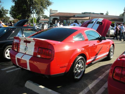 1998 Ford Crown Victoria - Rear three-quarter view of a red Shelby-style coupe with white racing stripes parked among other cars at a car show.