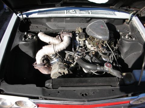 1998 Ford Crown Victoria - Open engine bay of a vintage car showing a turbocharger, heat-wrapped piping, carburetor and a finned chrome air cleaner.