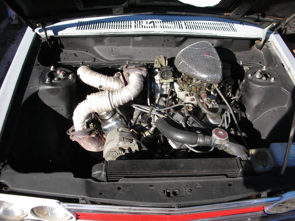 Engine bay of a vintage car with turbocharger, wrapped piping and chrome air cleaner