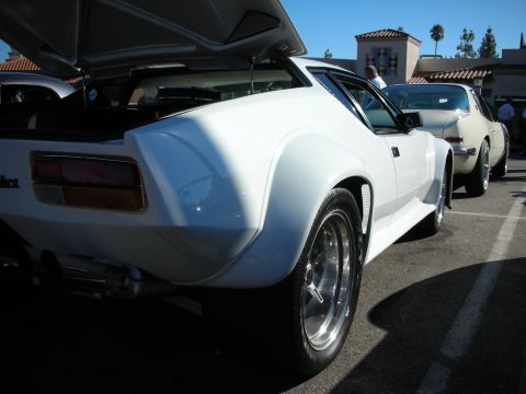 1998 Ford Crown Victoria - Rear three-quarter view of a white De Tomaso Pantera with its engine hatch open and polished wheels at a sunny car show.