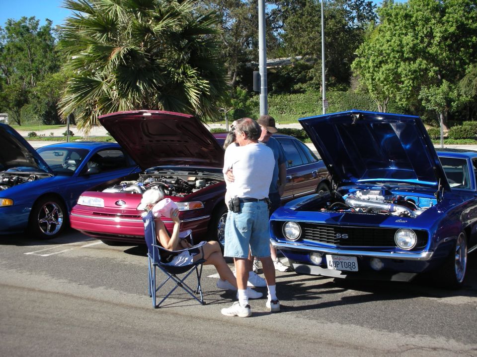 Blue Camaro SS and other cars with open hoods while spectators talk at a meet