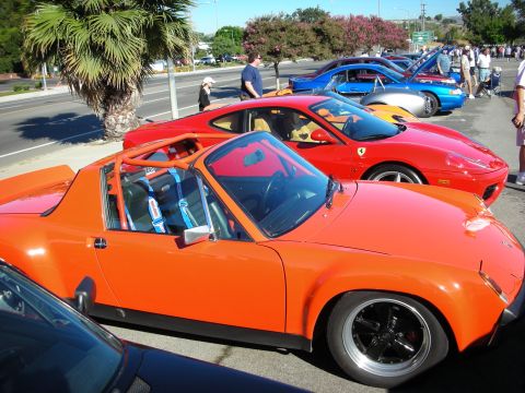 1998 Ford Crown Victoria - orange Porsche 914 targa with a roll bar parked next to a red Ferrari at a roadside car show.