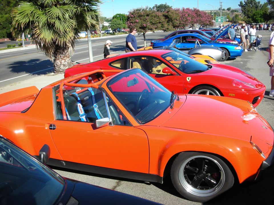 Orange Porsche 914 targa beside a red Ferrari at a roadside car meet