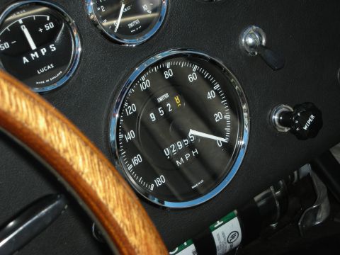 1998 Ford Crown Victoria - Close-up of a black Smiths speedometer and Lucas ammeter behind a wood-rimmed steering wheel in a classic roadster.
