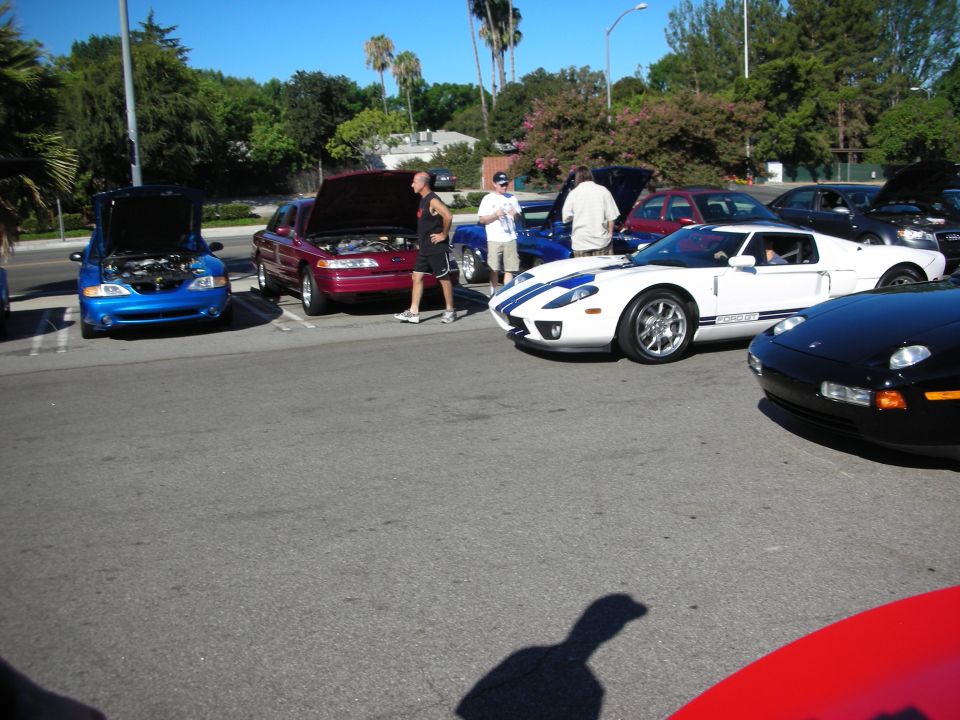 White Ford GT and black sports cars among show cars in a parking lot