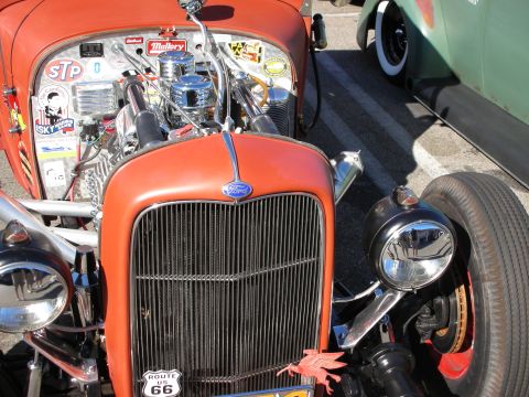 1998 Ford Crown Victoria - Front grille of an orange Ford hot rod with a chromed engine, vintage stickers and a Route 66 license plate.