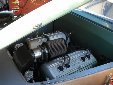 1998 Ford Crown Victoria - chromed V8 engine with finned Ardun valve covers and air filter sits under the lifted lid of a green hot rod.