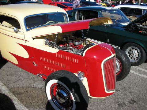 1998 Ford Crown Victoria - red and cream channeled hot rod roadster with a dual-carb V8 and wide whitewall tires at a car show.
