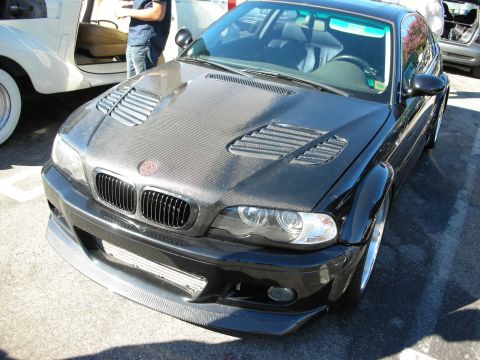 1998 Ford Crown Victoria - black BMW E46 M3 coupe with a carbon-fiber vented hood and front lip parked at an outdoor show.