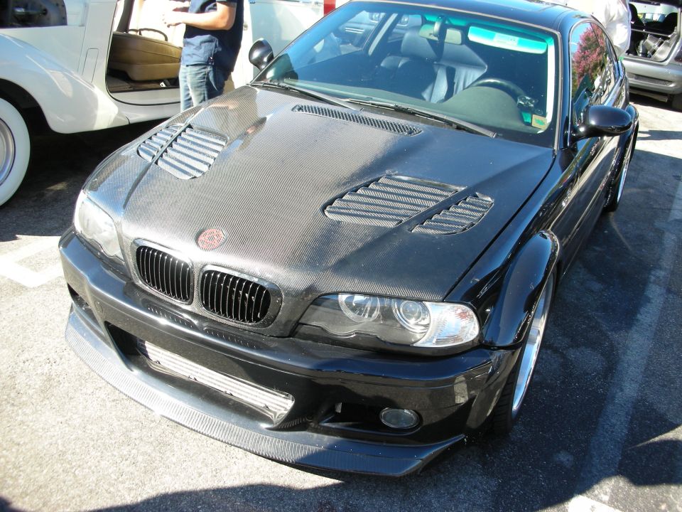 Black BMW M3 coupe with carbon hood and front lip at a car show