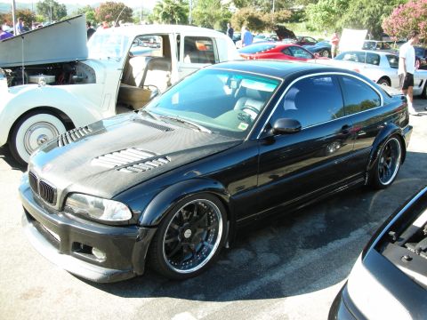 1998 Ford Crown Victoria - Side view of a lowered black BMW E46 M3 coupe on dark multi-spoke wheels among other show cars.