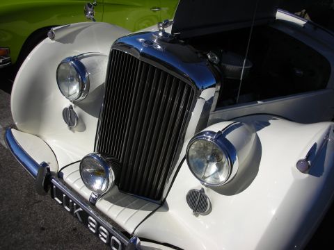 1998 Ford Crown Victoria - Close-up of the chrome vertical grille and round headlights of a white vintage British luxury car.