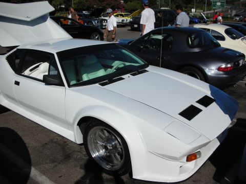 1998 Ford Crown Victoria - white wedge-shaped mid-engine sports car with its rear hatch raised, parked at a car show next to a dark convertible.
