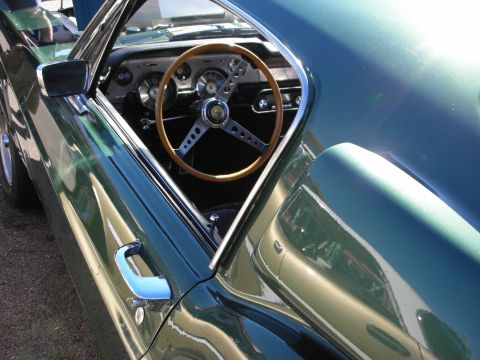 1998 Ford Crown Victoria - Through the side window of a metallic green fastback, a wood-rimmed steering wheel and round gauges are visible.