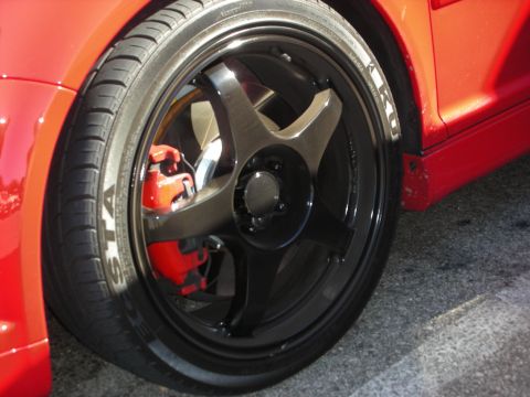 1998 Ford Crown Victoria - Close-up of a red sports car's front wheel showing a black five-spoke rim, red brake caliper, and Toyo tire.