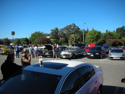 1998 Ford Crown Victoria - sunny car-show parking lot crowded with classic and modern cars and spectators, with an orange supercar at right.