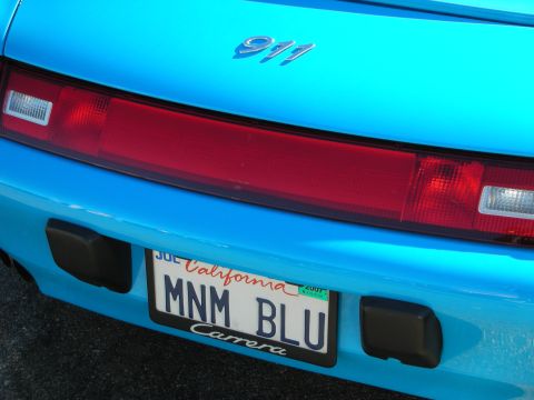 1998 Ford Crown Victoria - Rear of a light blue Porsche 911 Carrera showing the 911 badge, full-width taillight, and a California 'MNM BLU' plate.