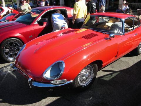 1998 Ford Crown Victoria - red Jaguar E-Type coupe with chrome wire wheels and covered headlights, parked at a car show with spectators behind.