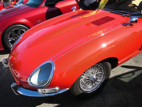 1998 Ford Crown Victoria - Close-up of a red Jaguar E-Type's long front fender, chrome covered headlight, and chrome wire wheel.