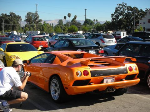 1998 Ford Crown Victoria - orange Lamborghini Diablo with raised rear wing and 'VT 60' plate parked in a packed car-show lot beside a yellow car.