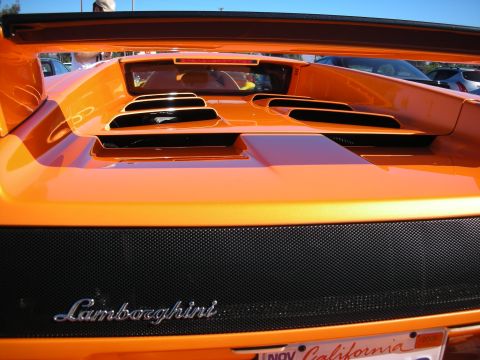 1998 Ford Crown Victoria - Close-up of an orange Lamborghini's rear deck showing engine intake vents, mesh grille, and the Lamborghini script badge.