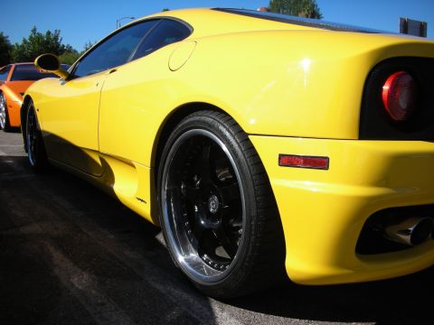 1998 Ford Crown Victoria - Rear three-quarter of a yellow Ferrari coupe on black multi-spoke wheels, with an orange supercar parked behind it.